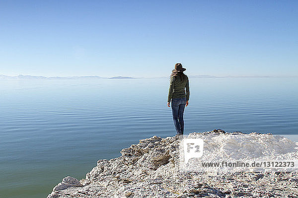 Rückansicht einer auf einem Felsen stehenden Frau auf Antelope Island vor klarem blauen Himmel