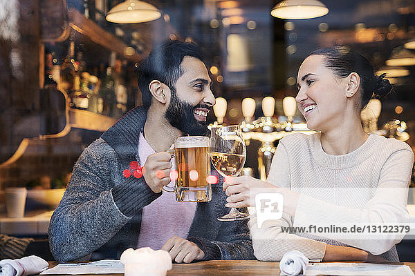 Happy couple toasting drinks seen through restaurant window