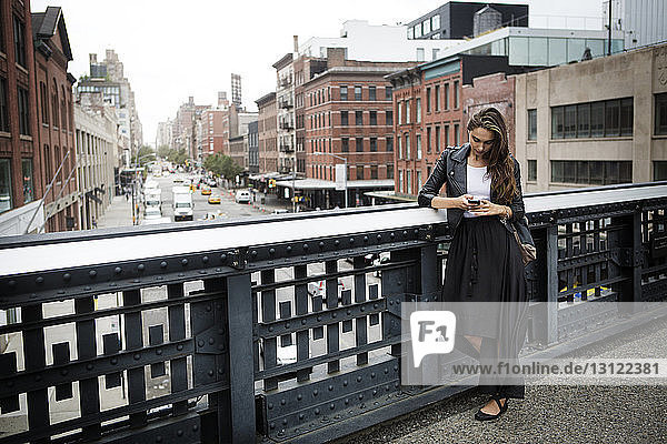 Frau benutzt Mobiltelefon  während sie auf einer Brücke in der Stadt steht