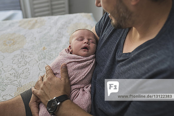 Ausgeschnittenes Bild eines Vaters  der eine neugeborene Tochter trägt  während er auf dem Bett sitzt