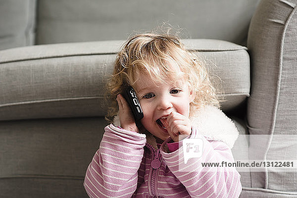 Girl talking on mobile phone by armchair at home