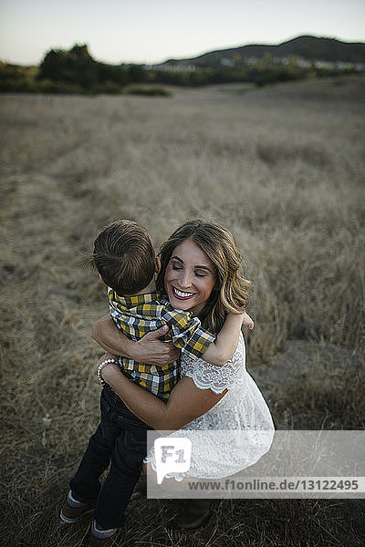 Hochwinkelansicht einer Mutter  die ihren Sohn umarmt  während sie auf dem Feld kauert