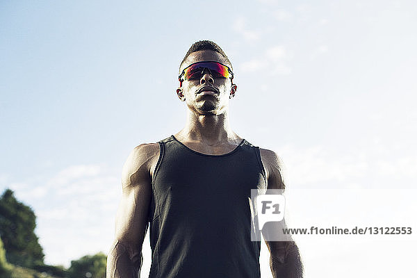 Niedriger Blickwinkel eines selbstbewussten Sportlers mit Sonnenbrille gegen den Himmel