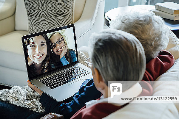 Videokonferenz eines älteren Ehepaares mit Enkelinnen über einen Laptop zu Hause