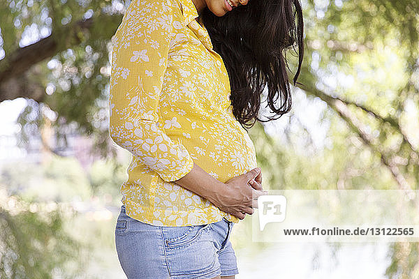 Midsection of pregnant woman with hands on stomach standing at park