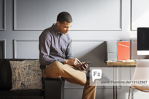 Geschäftsmann benutzt Tablet-Computer  während er im Büro auf dem Sofa sitzt