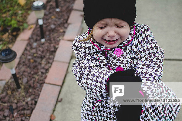 Hochwinkelaufnahme eines Mädchens in warmer Kleidung  das weint  während es auf dem Bürgersteig steht