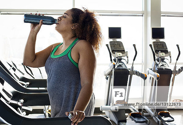 Frau trinkt Wasser  während sie im Fitnessstudio auf dem Laufband steht
