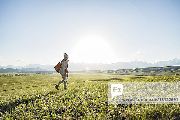 Rear view of female hiker walking on grassy field against clear sky