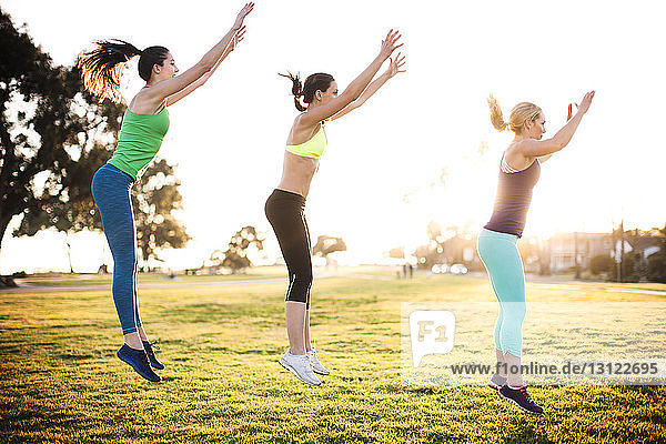 Friends exercising on grassy field on sunny day