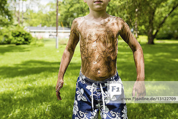 Mitschnitt eines schmutzigen Jungen ohne Hemd  der auf einem Grasfeld im Hinterhof steht
