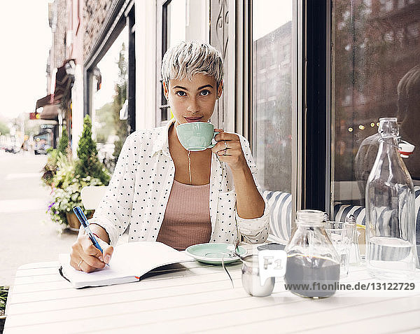Portrait of woman holding coffee cup and pen at sidewalk cafe