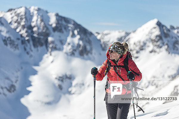 Nachdenkliche Frau hält Skistöcke  während sie vor schneebedeckten Bergen steht
