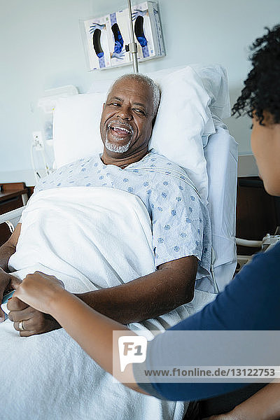 Glücklicher Vater spricht mit Tochter  während er sich auf der Krankenhausstation ans Bett lehnt