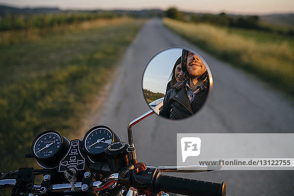Spiegelung eines jungen Paares auf einem Motorrad im Seitenspiegel