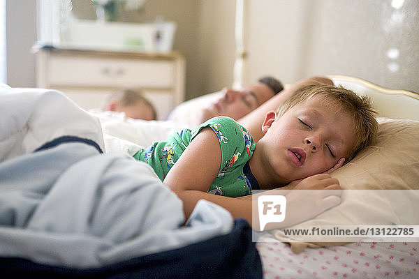 Father and sons sleeping on bed at home