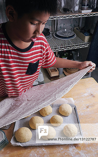 Hochwinkelaufnahme eines Jungen  der zu Hause auf der Küchentheke Brötchen backt