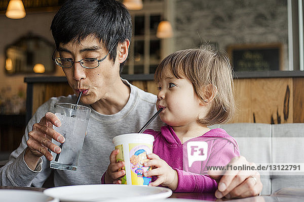 Father with daughter having drinks while sitting at table in cafe