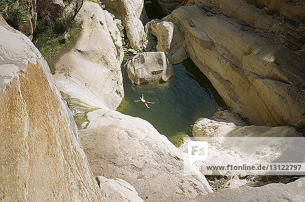 Fernansicht eines Mannes beim Sonnenbaden in einem Teich inmitten von Felsen