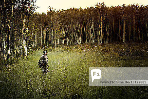 Hunter with bow and arrow walking in forest
