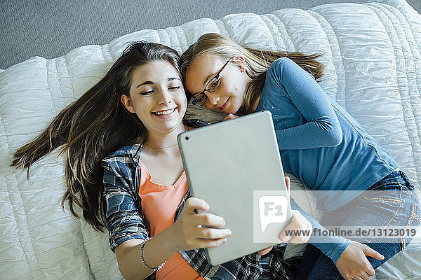 Hochwinkelansicht von glücklichen Schwestern mit einem Tablet-Computer  während sie zu Hause auf dem Bett liegen