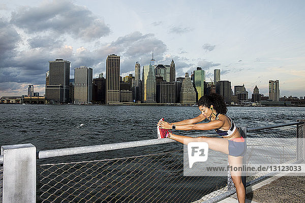 Weibliche Sportlerin übt bei Sonnenuntergang am Fluss gegen den Himmel in der Stadt