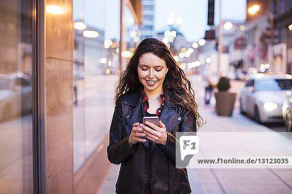 Junge Frau benutzt Smartphone  während sie auf einem Fußweg an Gebäuden vorbei geht