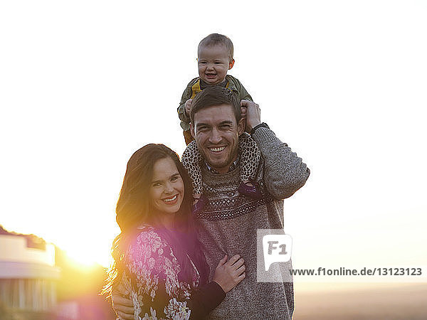 Porträt glücklicher Eltern mit niedlicher Tochter  die bei Sonnenuntergang am klaren Himmel stehen
