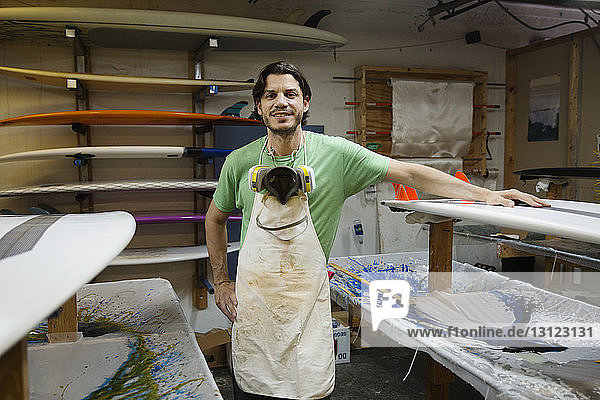 Porträt eines lächelnden Mannes  der im Workshop an Surfbrettern steht