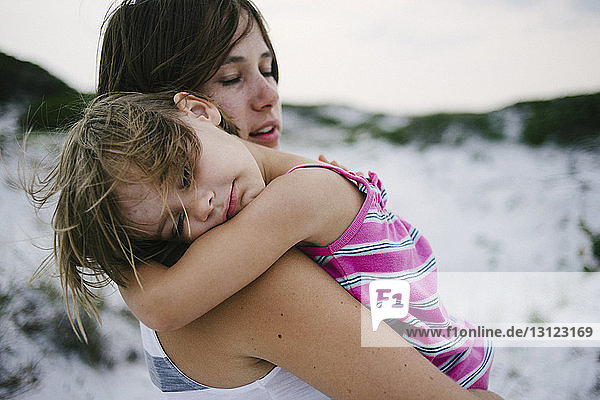 Mutter trägt Tochter  die am Strand schläft