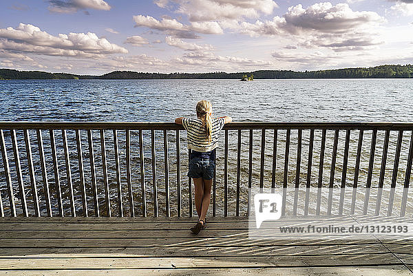 Rear view of girl standing on jetty by railing over lake and looking at view