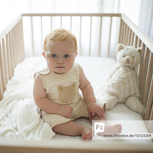 Portrait of cute baby boy sitting in crib at home