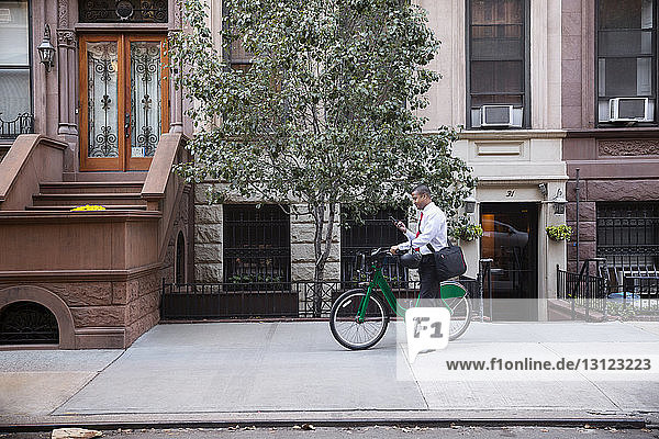 Geschäftsmann benutzt Mobiltelefon  während er mit dem Fahrrad auf dem Fußweg steht
