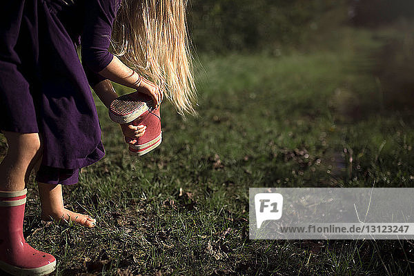 Mädchen entfernt Schmutz von Gummistiefeln auf dem Spielfeld im Park