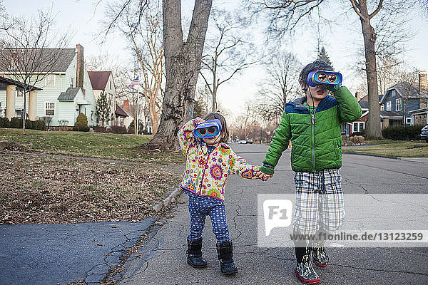 Geschwister  die beim Spielen auf der Straße beim Blick durch das Fernglas Händchen halten