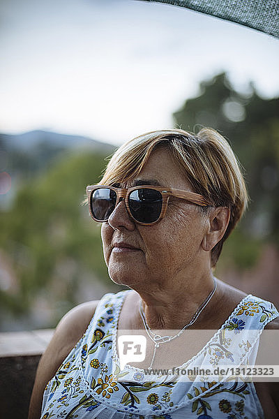 Close-up of senior woman wearing sunglasses while standing on building terrace against sky