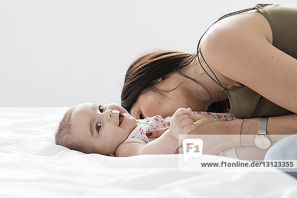 Side view of mother playing with smiling daughter lying on bed at home