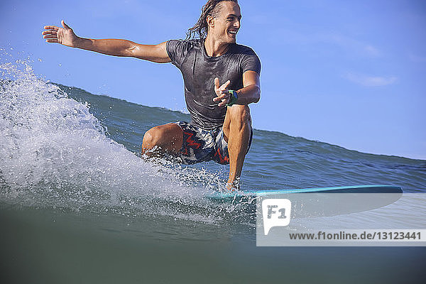 Lächelnder Mann surft auf dem Meer vor blauem Himmel