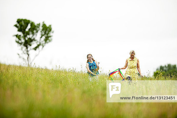Happy mother and daughter walking on grassy field against clear sky
