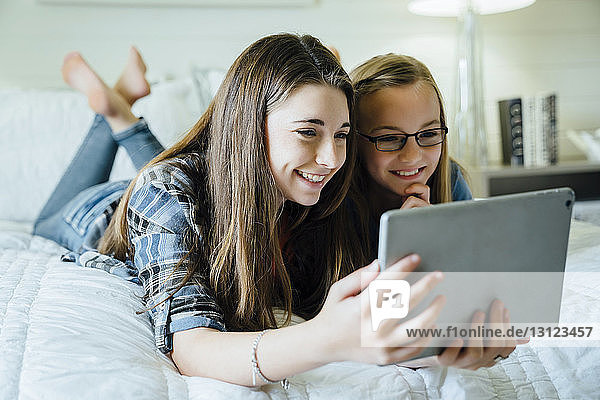 Glückliche Schwestern mit Tablet-Computer im Schlafzimmer
