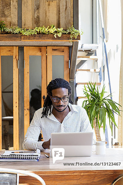 Konzentrierter junger Geschäftsmann mit Laptop am Schreibtisch im Kreativbüro