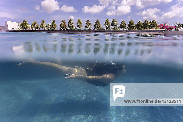 Frau schwimmt in voller Länge unter Wasser gegen bewölkten Himmel