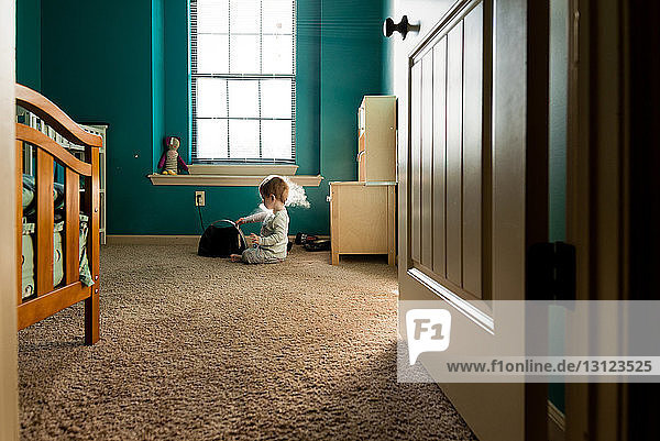 Junge spielt mit Dampfmaschine  während er zu Hause auf dem Teppich sitzt und durch die Tür gesehen wird