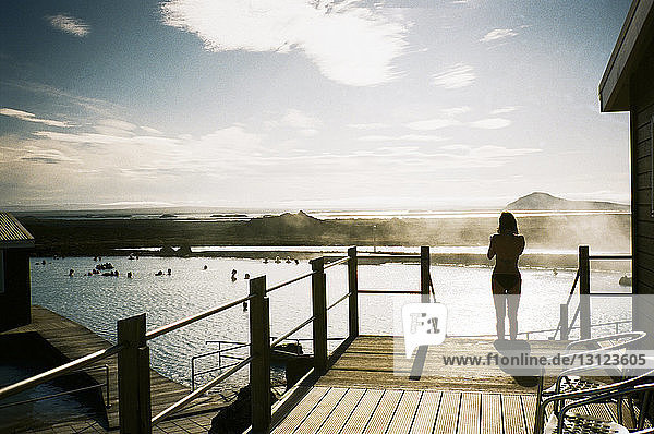 Rear view of woman standing on steps by lake against sky