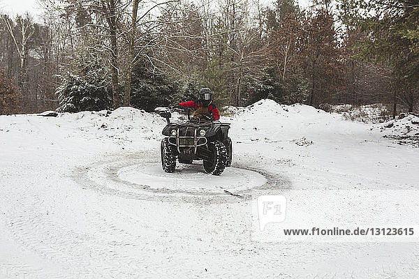 Teenage boy riding quadbike on snowy field