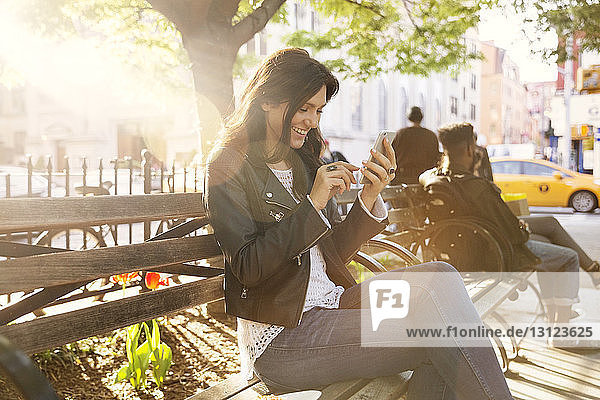 Glückliche Frau benutzt ein Smartphone  während sie in der Stadt auf einer Bank sitzt