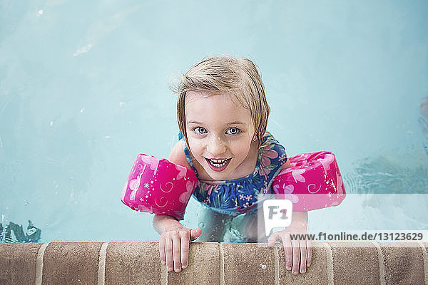 Portrait of happy girl wearing water wings swimming in pool