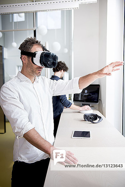 Businessman examining virtual reality simulator while coworker using computer in office