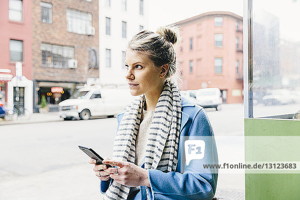Junge Frau schaut weg  während sie in der Stadt ein Smartphone benutzt