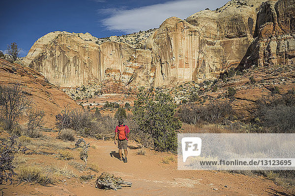 Rear view of hiker with backpack walking on desert against rock formations